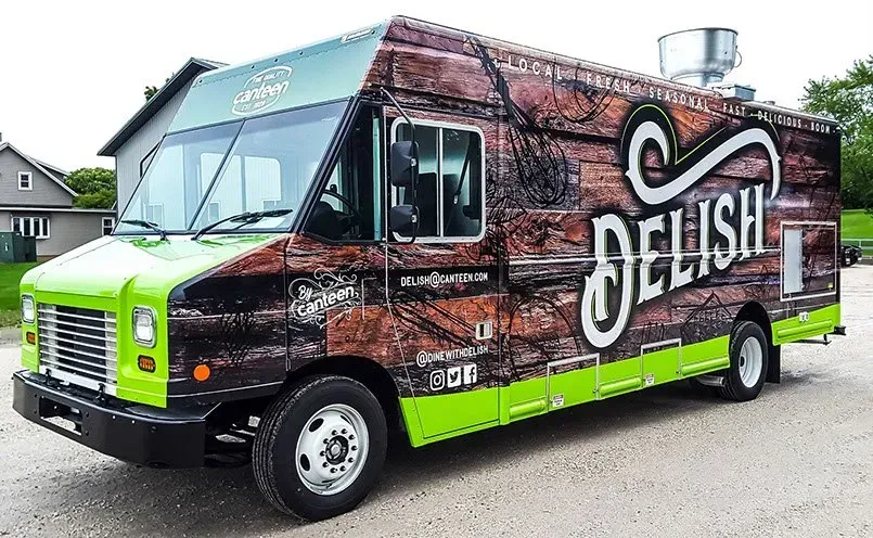 A green and brown food truck is parked on the side of the road.