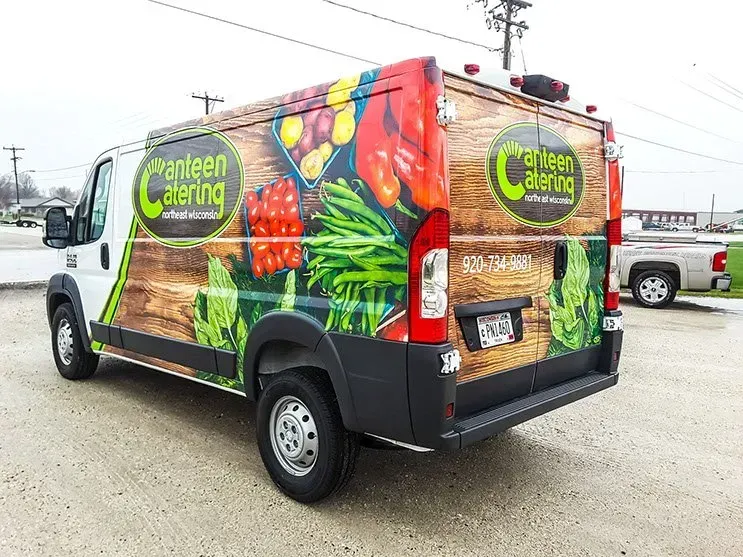 A van with a vegetable wrap on it is parked in a parking lot.
