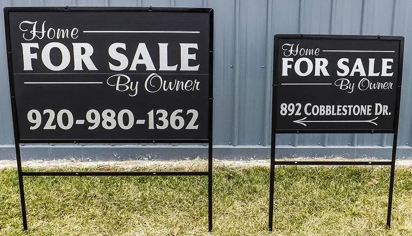 Two for sale signs are sitting on the grass in front of a building.