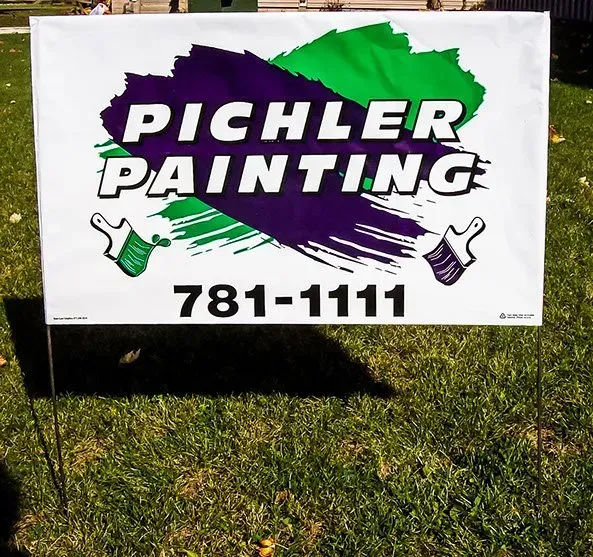 A sign for pichler painting is sitting in the grass