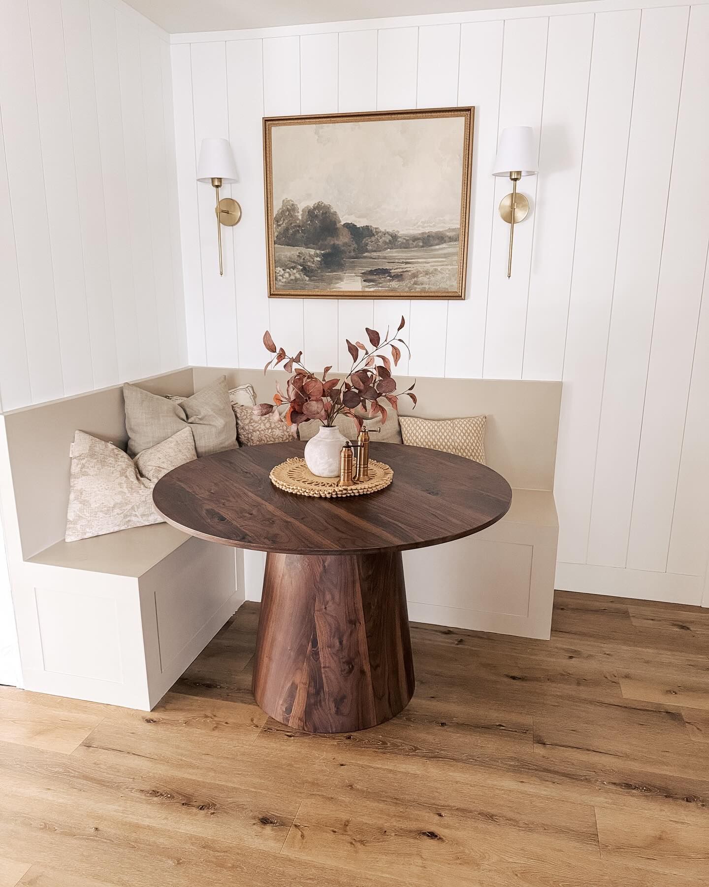 Cozy dining nook with round wooden table, built-in bench, framed artwork, and wall sconces.