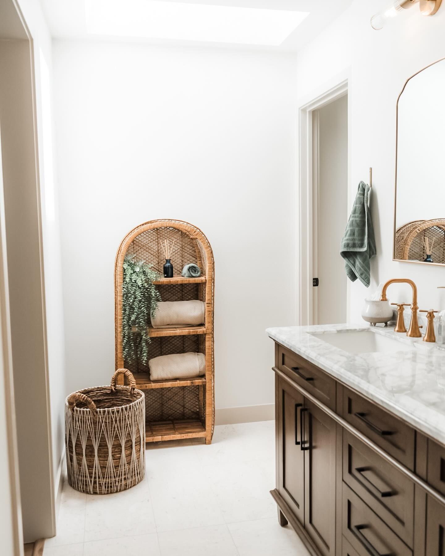 Bathroom with wicker shelving, dark wood vanity, white walls, and a large mirror.