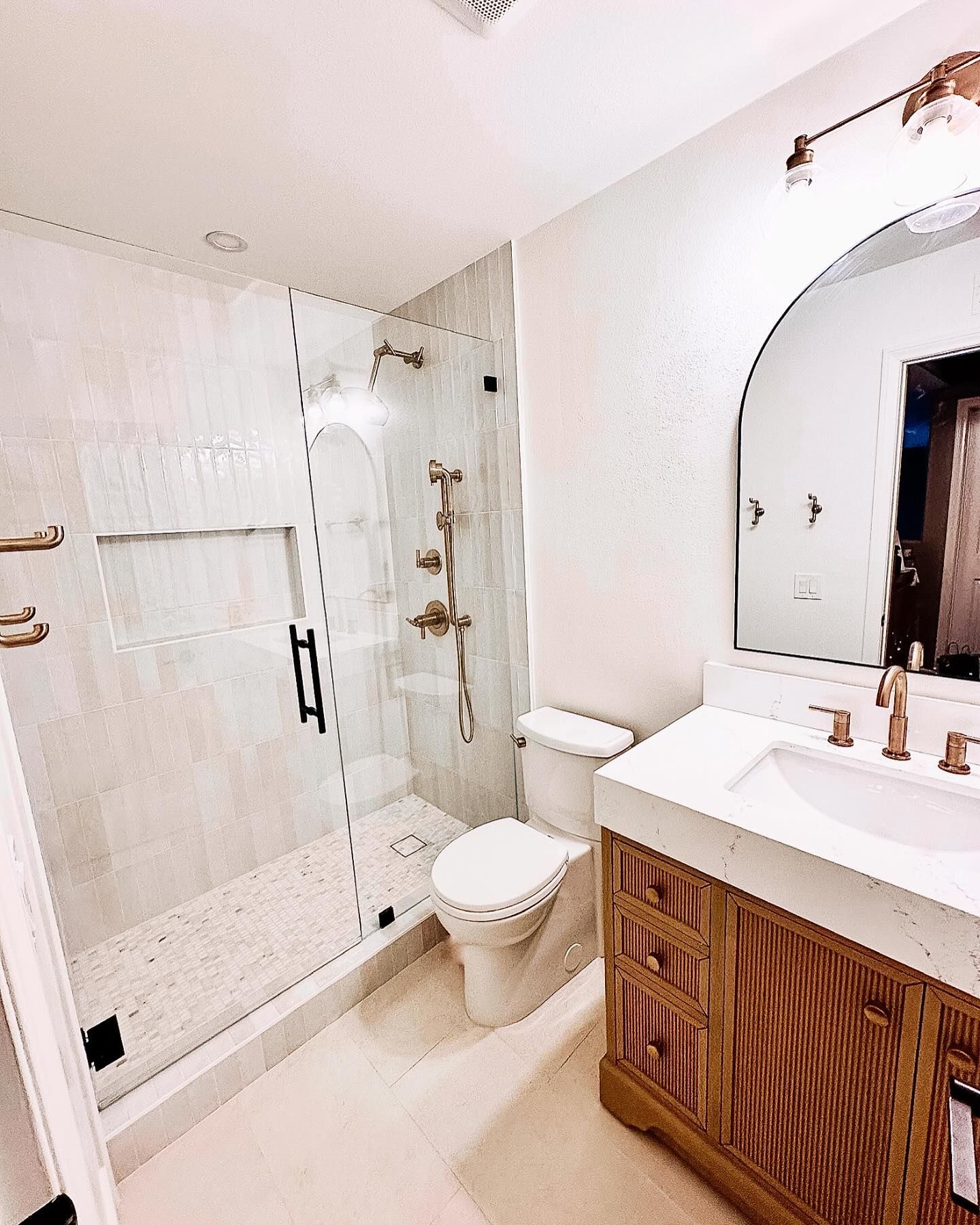 Bathroom with a glass shower, white walls, wood vanity, and gold fixtures.