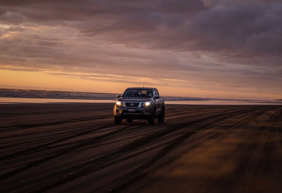Fully insured pickup truck driving along a sandy beach shore at sunset