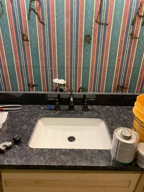 Bathroom sink with dark countertop, striped wallpaper, and a soap dispenser on the right.