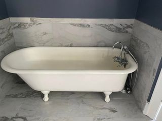 White clawfoot bathtub with faucet in a marble-tiled bathroom corner.
