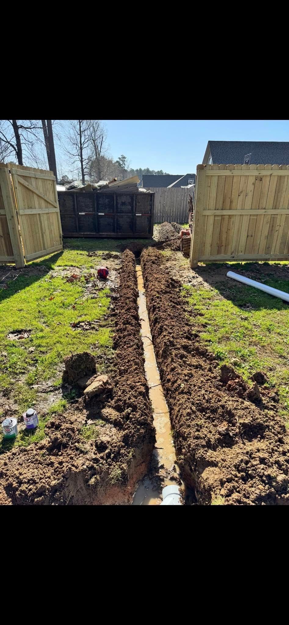 Mud path between wooden fences leading to a gate in a sunny yard