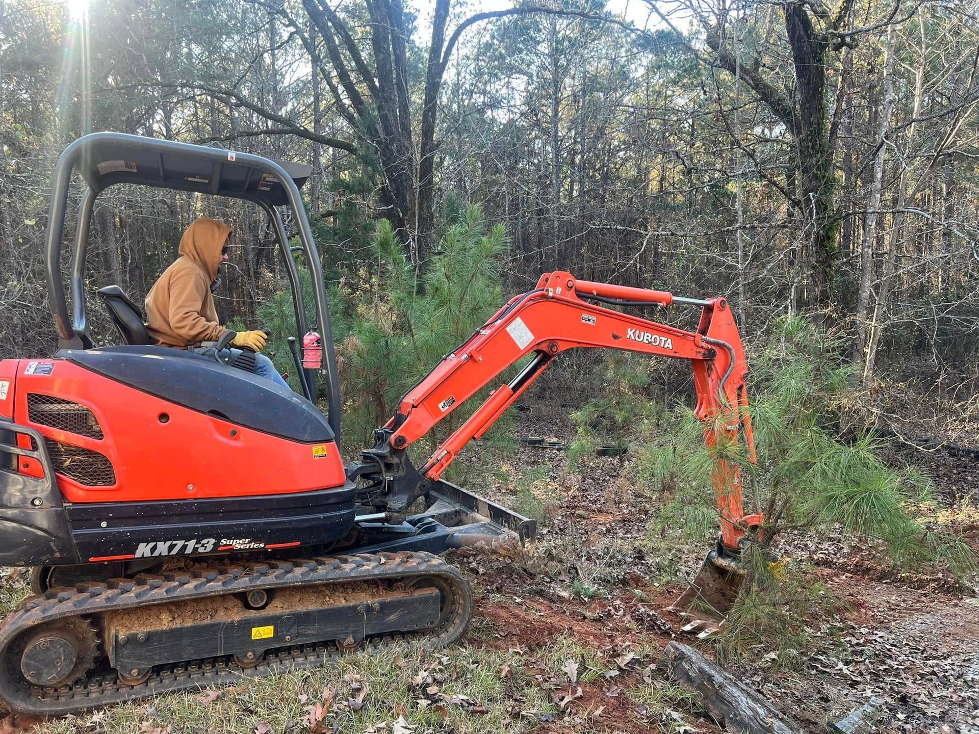 Orange mini excavator clearing brush in a wooded area