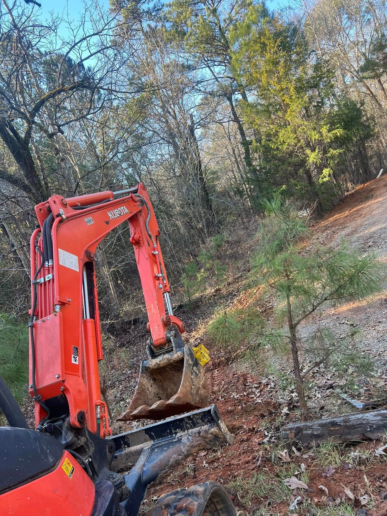 Orange excavator digging leaves and dirt on a wooded hillside in autumn