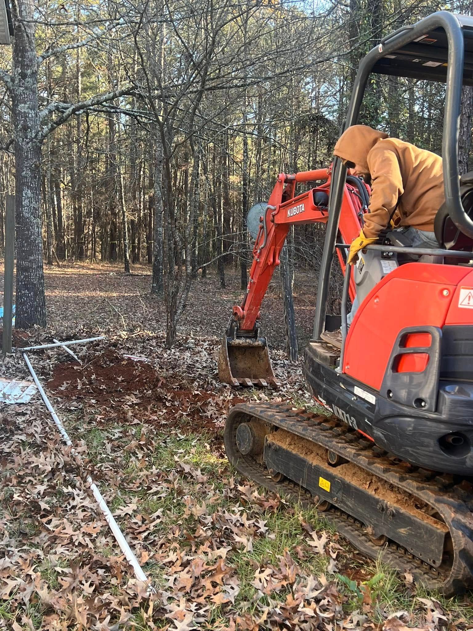 Orange excavator clearing leaves in a wooded area with an operator in the cab