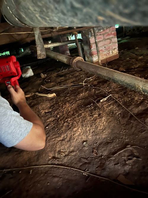 Person holding a red flashlight under a vehicle in a dark, muddy area