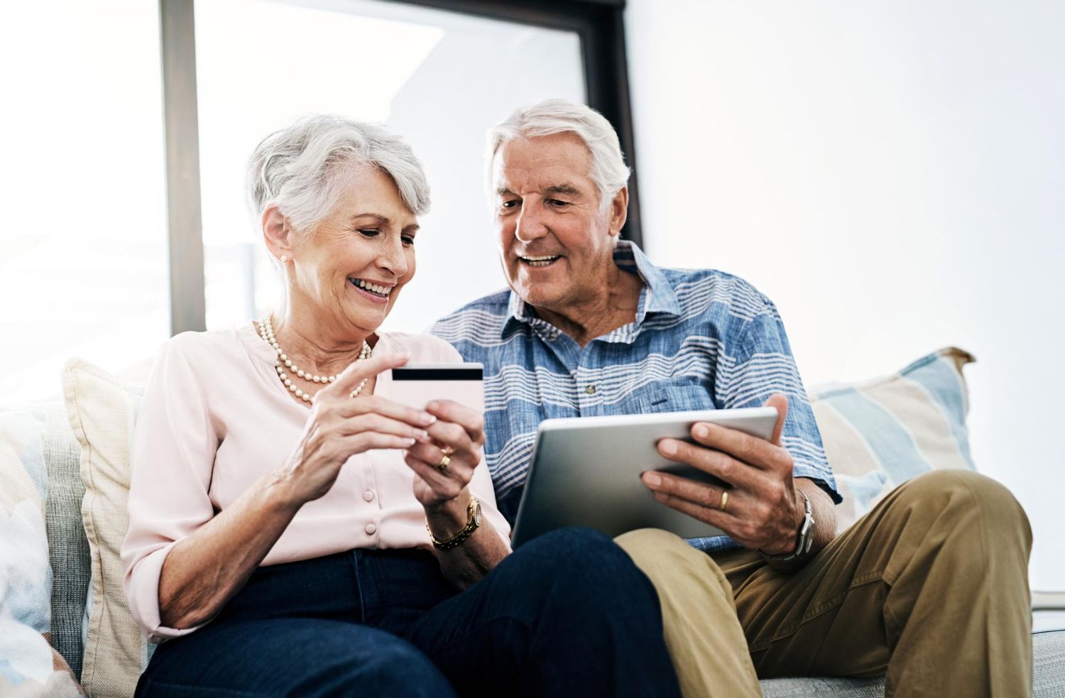 Two people sitting on a couch, smiling while using a credit card and tablet