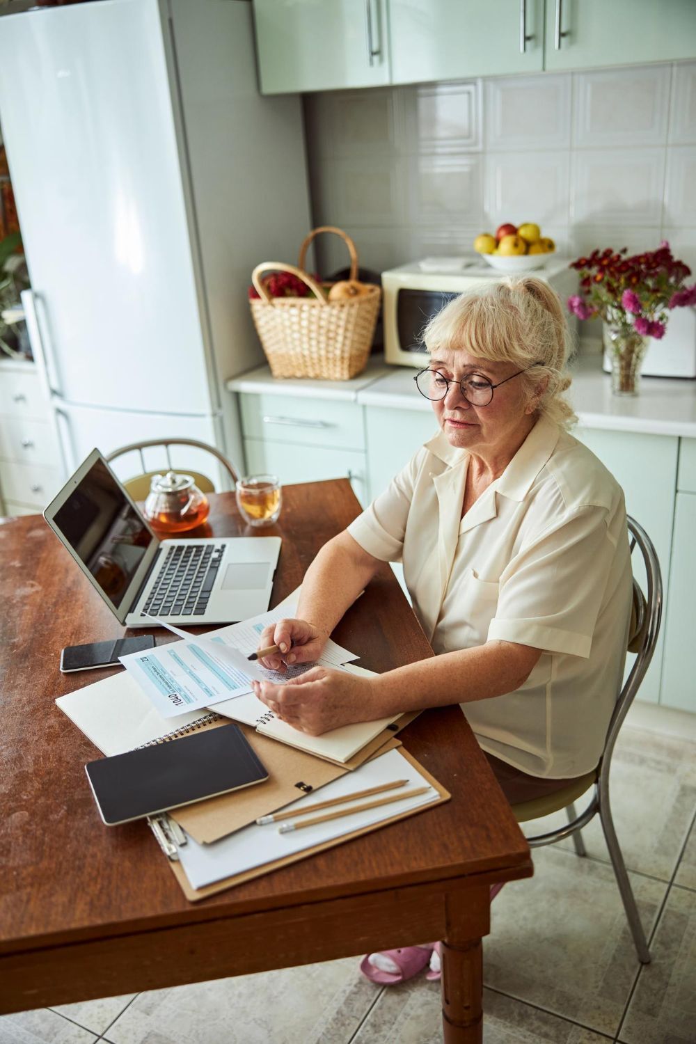 Woman sitting at a kitchen table reviewing papers beside a laptop and coffee