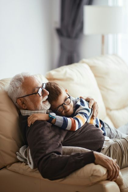 Elderly man holding a sleeping child on a sofa in a bright living room