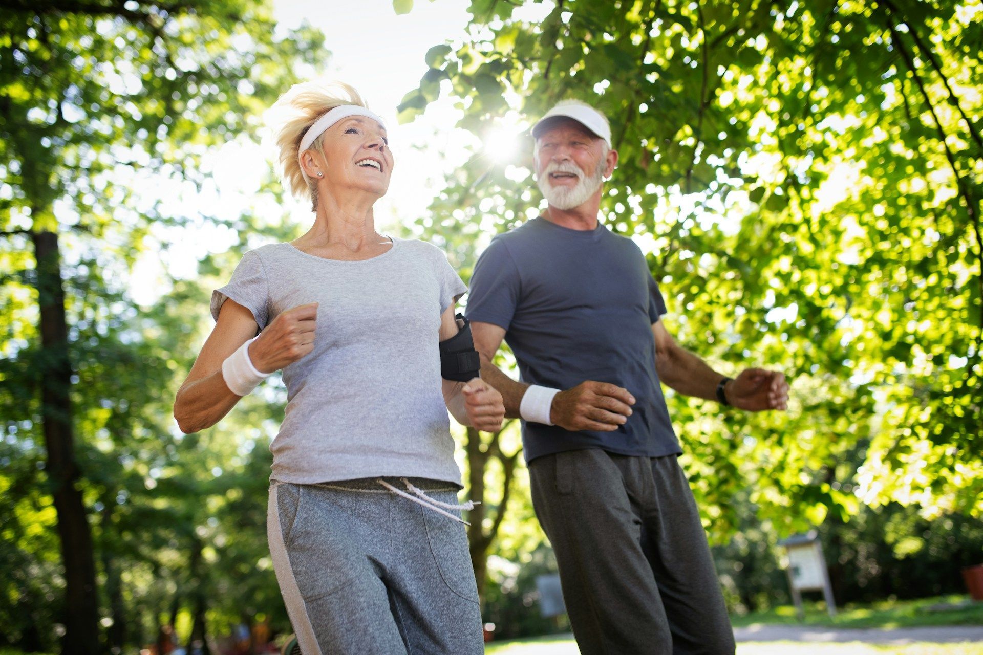 Two adults jogging on a tree-lined path, smiling in bright sunlight