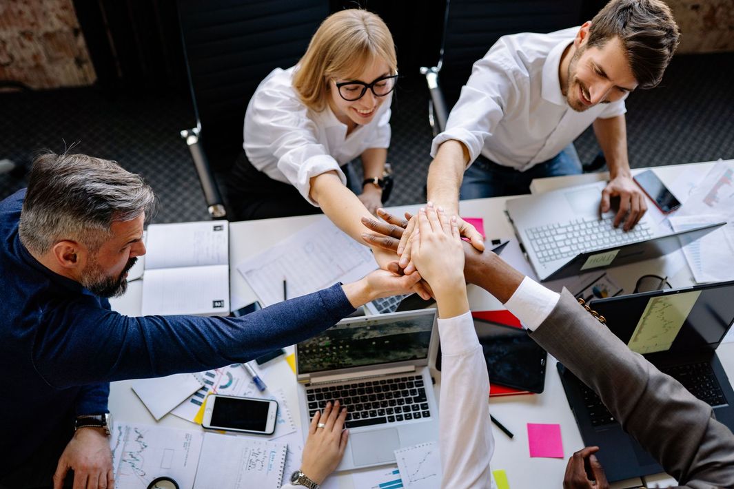 Team of coworkers high-fiving over laptops and papers at a meeting table