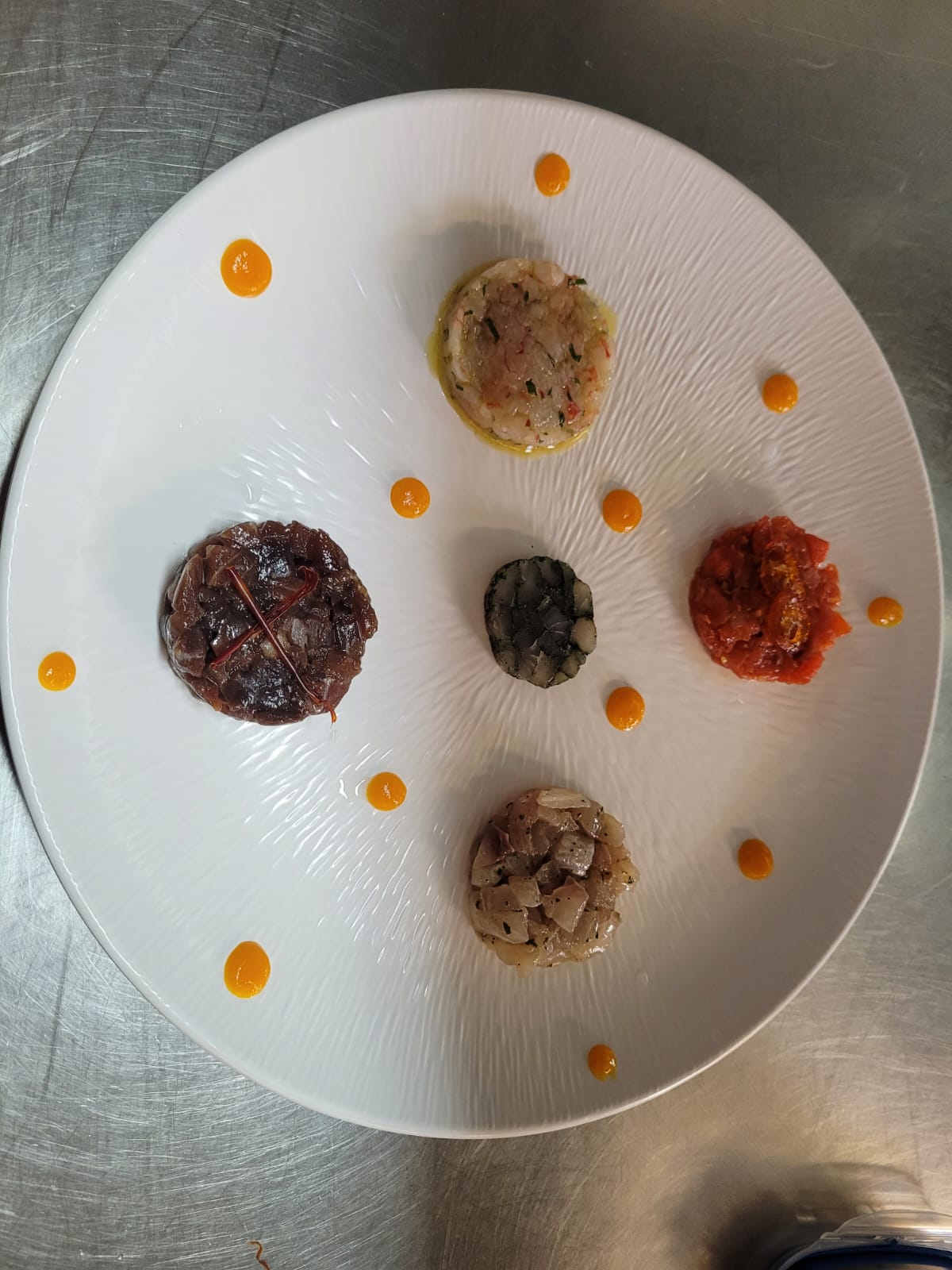 Stuzzichini gourmet con gocce di salsa all'arancia su un piatto rotondo bianco.
