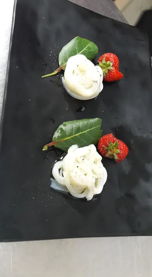 Due piccole volute di crema bianca con foglie verdi e fragole su un vassoio nero.