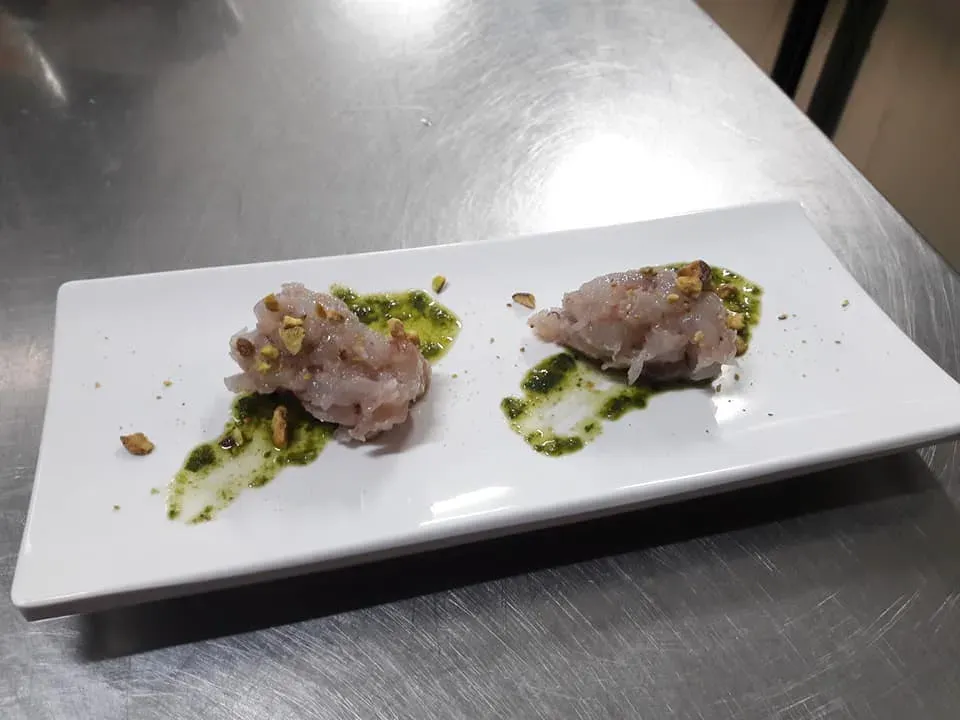 Due piccoli pezzi di cibo su un piatto rettangolare bianco con salsa verde su un tavolo di metallo.