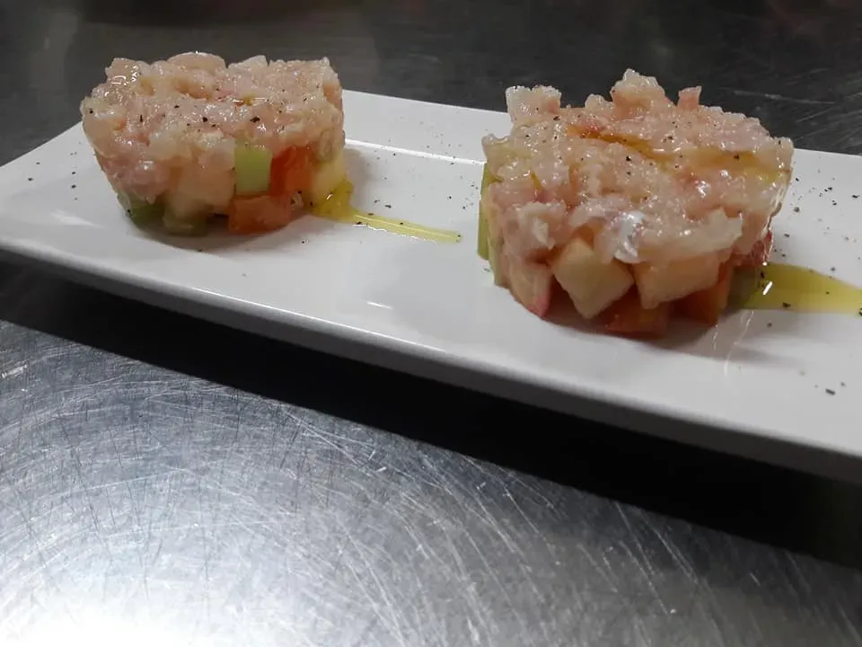 Due piccole porzioni di tartare di pesce a dadini su un piatto rettangolare bianco con un filo di salsa.