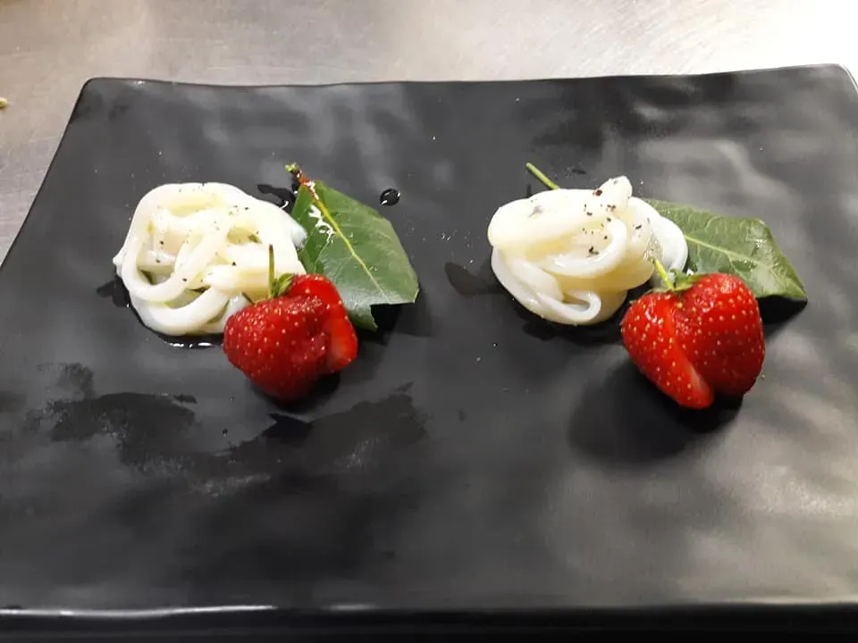 Due piccoli dessert alla fragola e panna su un piatto nero con foglie di menta verde.