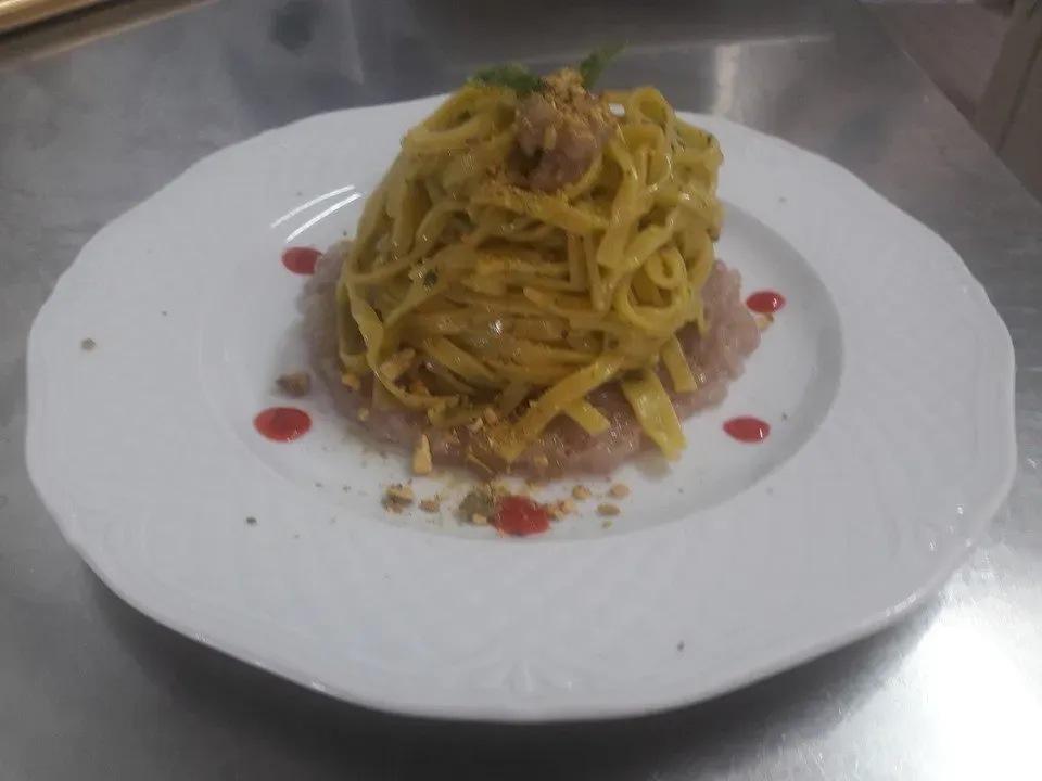 Pasta gialla condita con carne e guarnita con salsa rossa, servita su un piatto bianco.