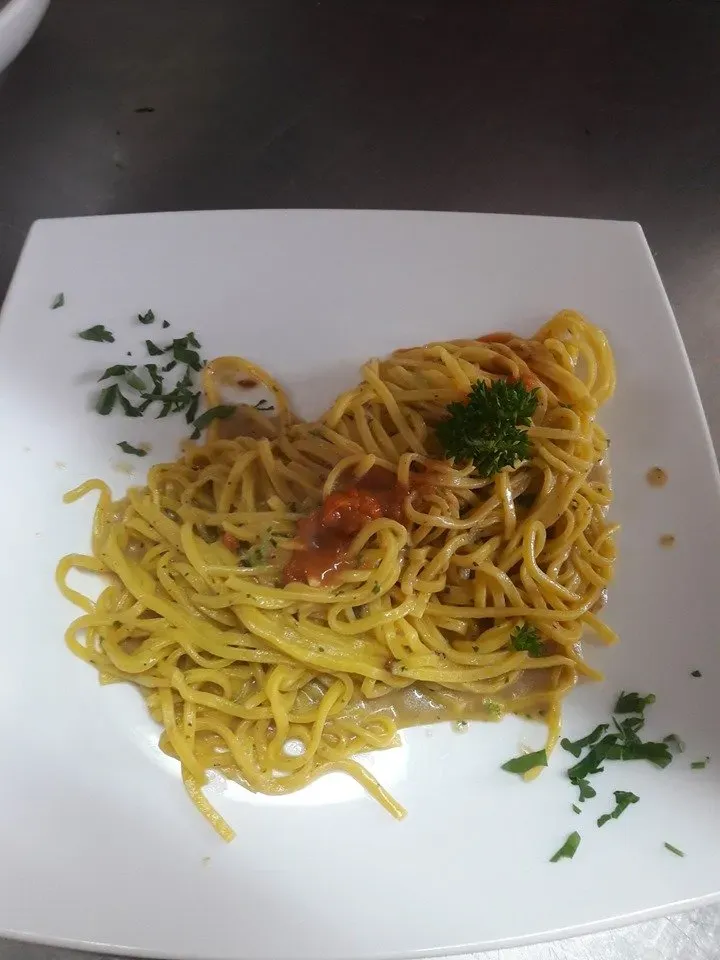Piatto di spaghetti gialli al sugo di pomodoro ed erbe aromatiche su un piatto quadrato bianco.