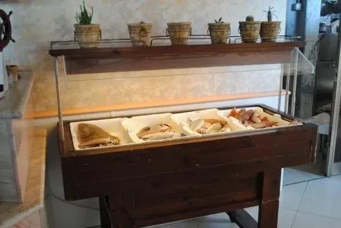 Vetrina con assortimento di pane e pasticcini su un tavolo di legno, sormontata da piccole piante in vaso.