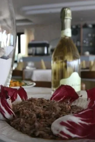 Una bottiglia di vino bianco dietro un piatto di risotto guarnito con petali di radicchio rosso in un ristorante.