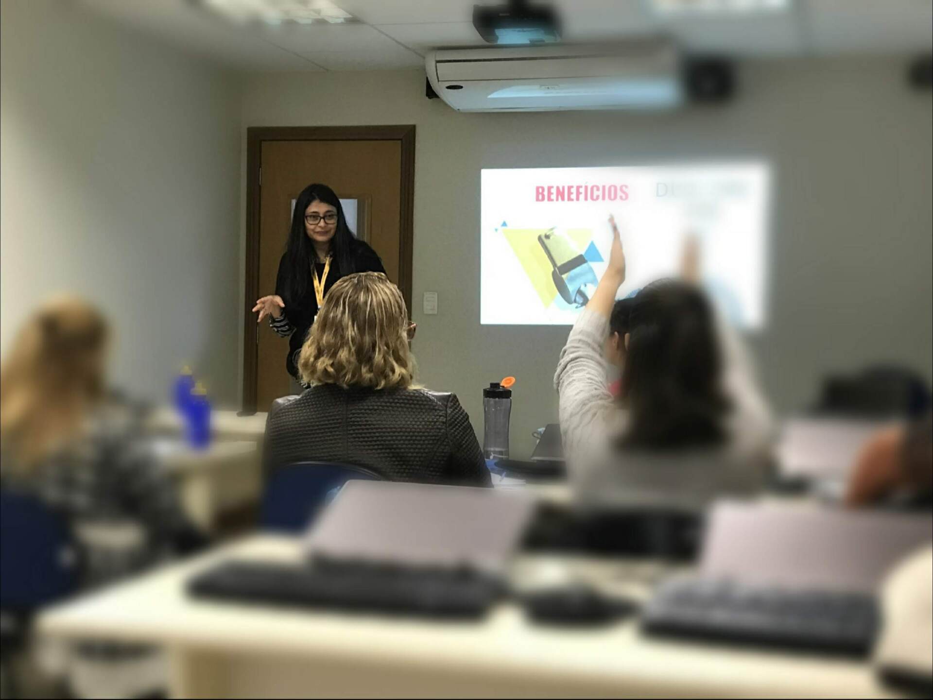 Mulher apresentando um slideshow, pessoa levantando a mão em uma sala de aula.