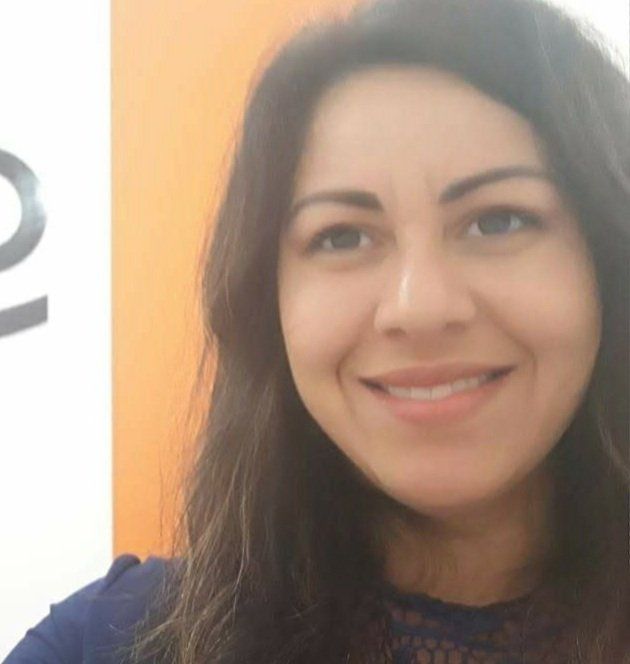 Mulher de cabelos castanhos sorrindo, fundo laranja desfocado.