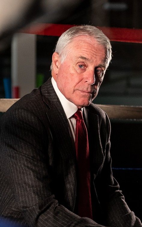 Man in a dark suit and red tie seated indoors, looking at the camera.