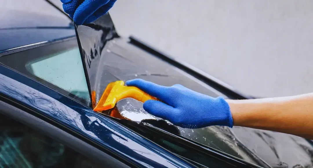 A person is applying tinted glass to a car window.