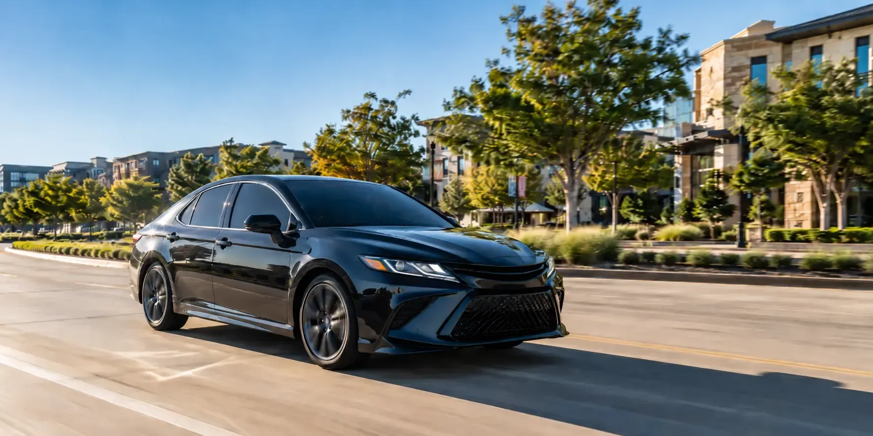 Black sedan with dark tinted windows driving on a sunny road in Frisco, Texas