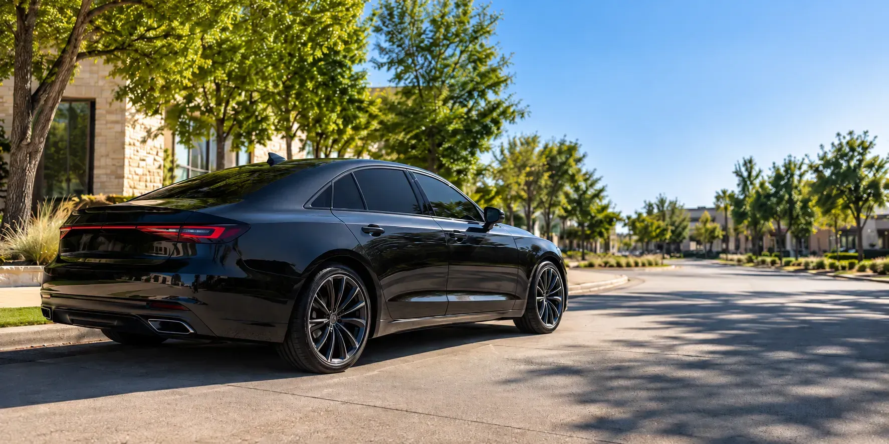 Sleek black sedan with dark window tint parked on a sunny tree-lined street in Richardson, Texas
