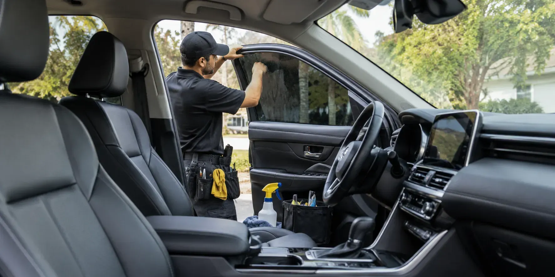 Clean modern car interior prepared for mobile window tinting, with a professional technician working on the side window.
