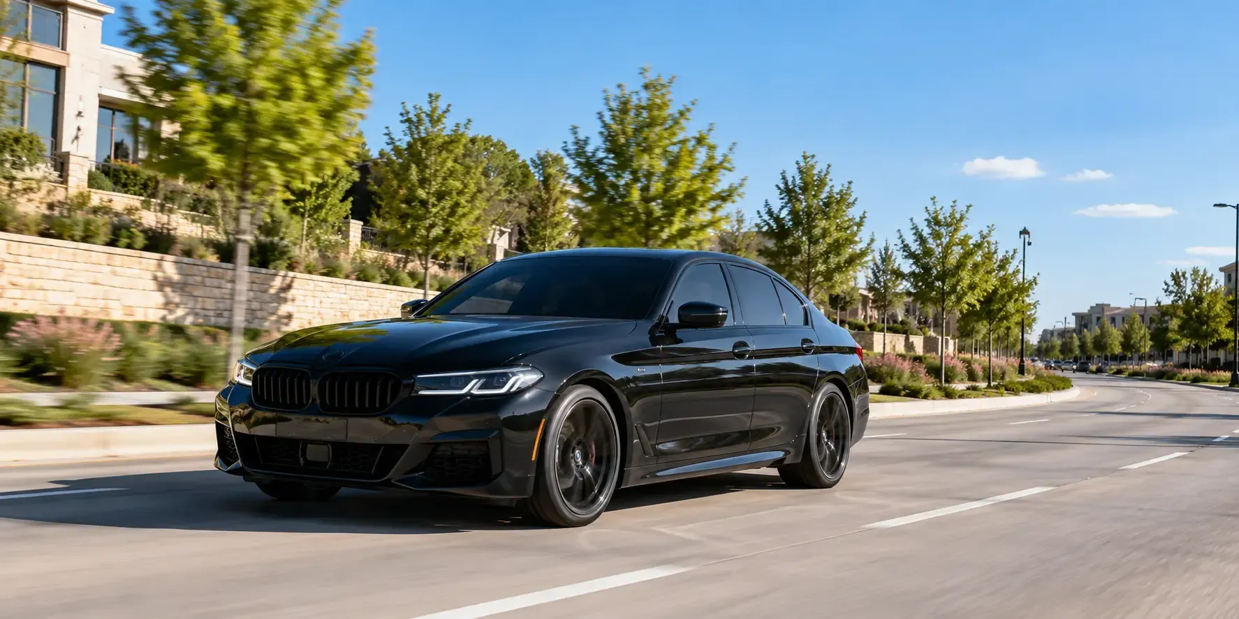 Sleek black sedan with dark tinted windows driving on a sunny road in Frisco, Texas.