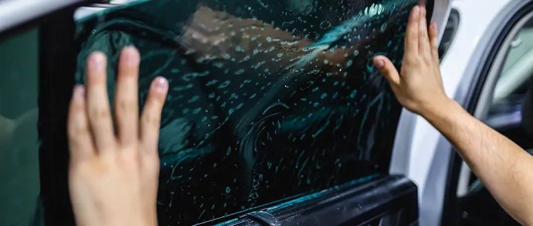 A man is applying tinted window film to a car window.
