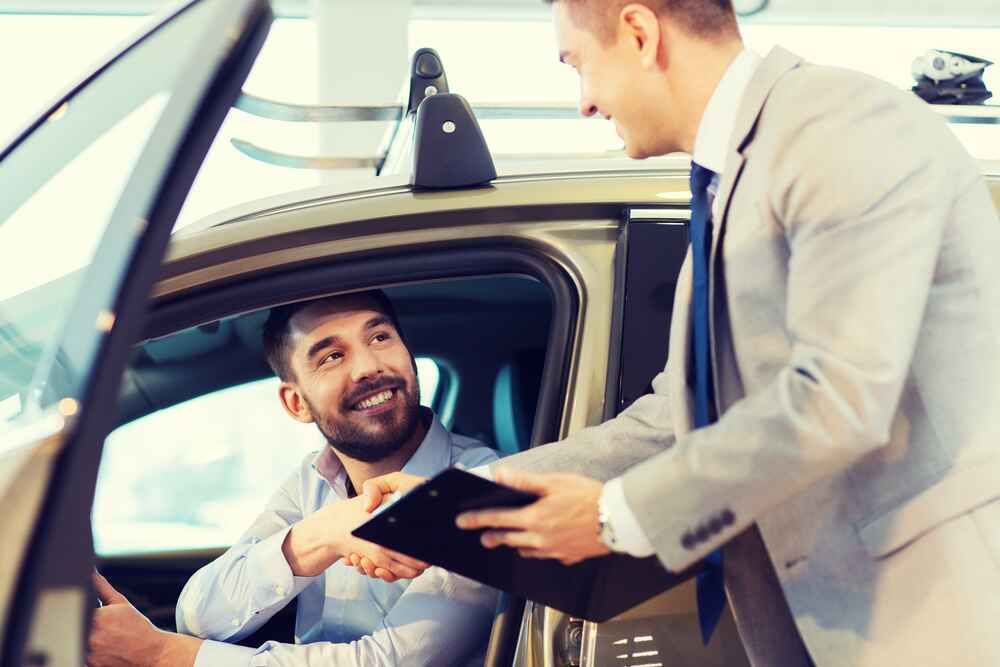 A Man is Shaking Hands With a Car Salesman in a Car Showroom — Skids Mechanical Services Pty Ltd in Wagga Wagga, NSW