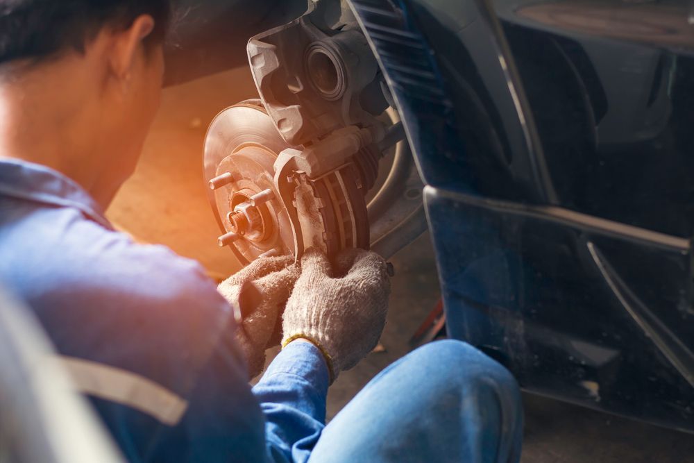 A Man is Kneeling Down Fixing a Brake Pad on a Car — Skids Mechanical Services Pty Ltd in Wagga Wagga, NSW