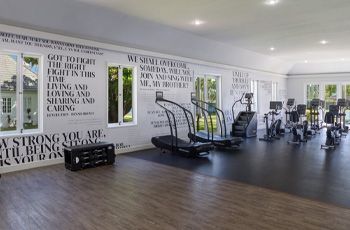 Modern gym with treadmills, exercise bikes, and black flooring under bright lights.