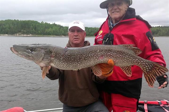 Two men holding a large northern pike on a boat