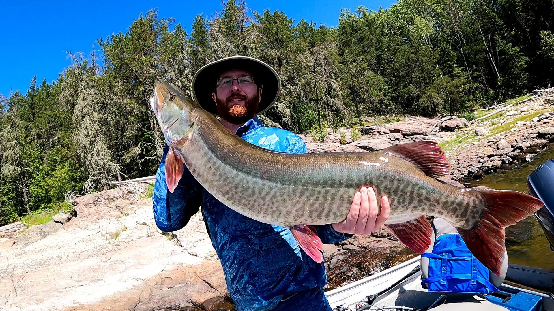 A man is holding a large 47-inch muskie fish in his hands.