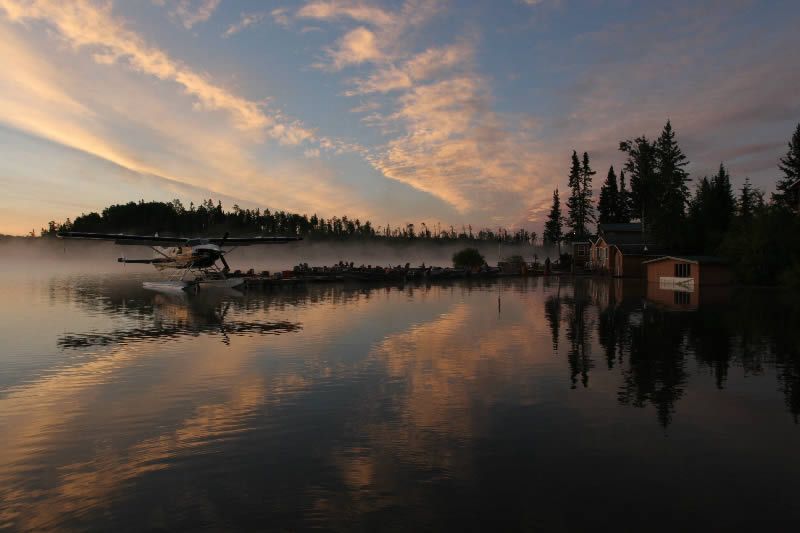 A seaplane is flying over a lake at sunset.