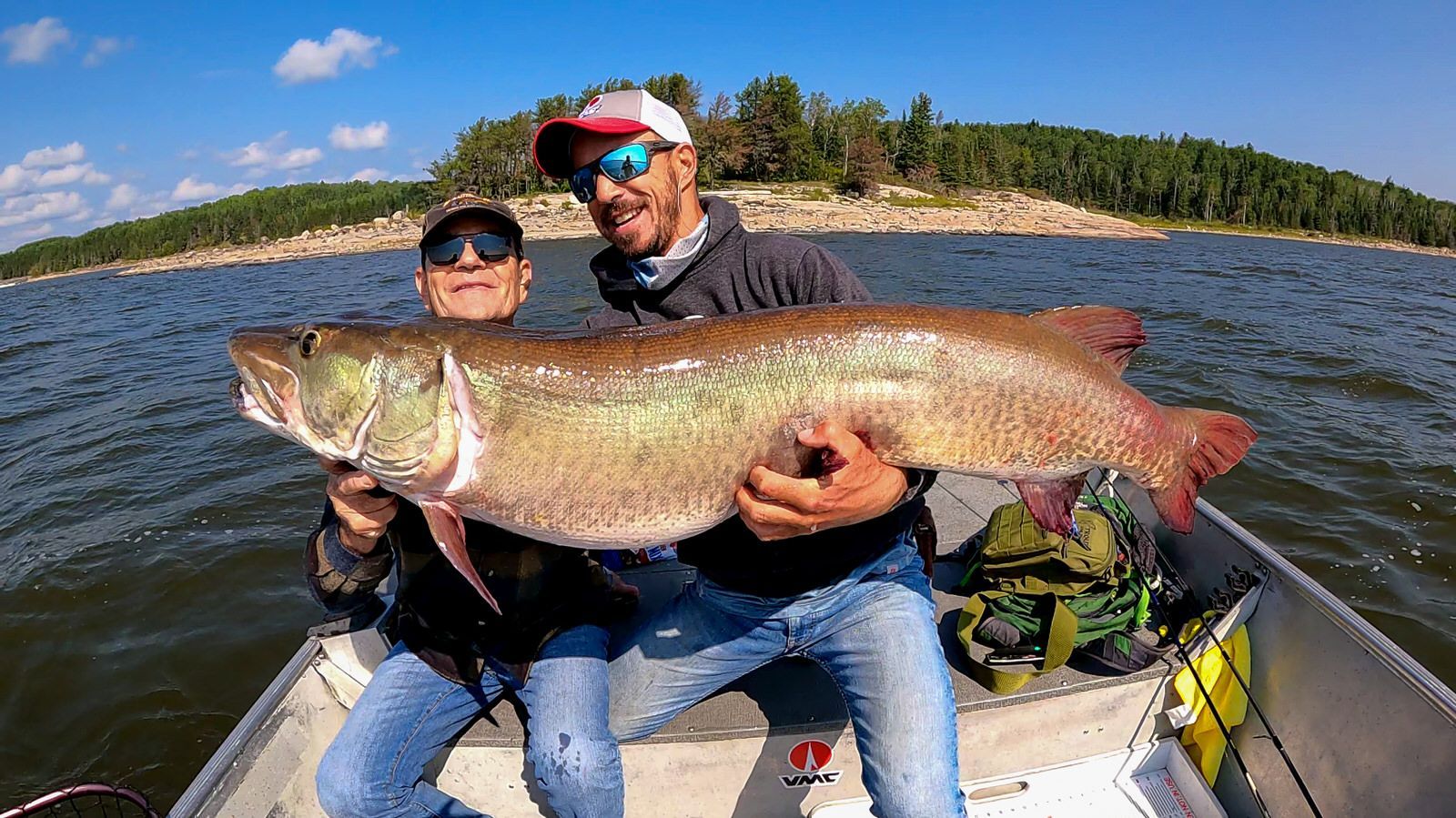 Two men are sitting in a boat holding a large muskie.