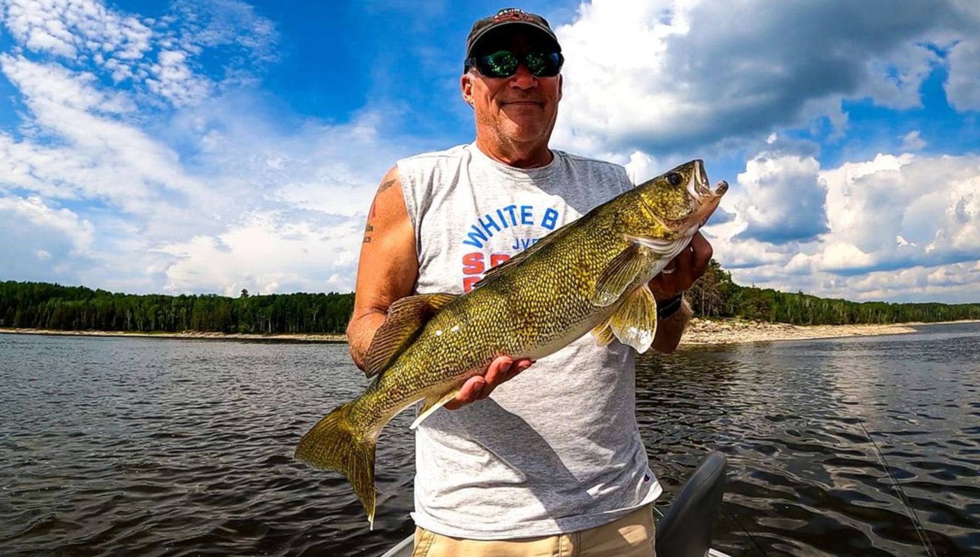 A man in a boat is holding a large walleye fish in his hands.