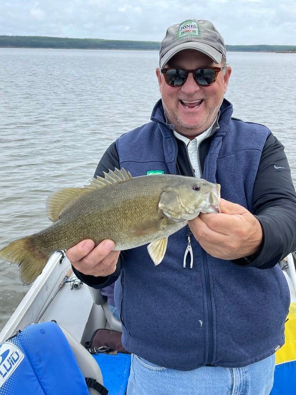 Philip is holding a smallmouth bass  in his hands on a boat.