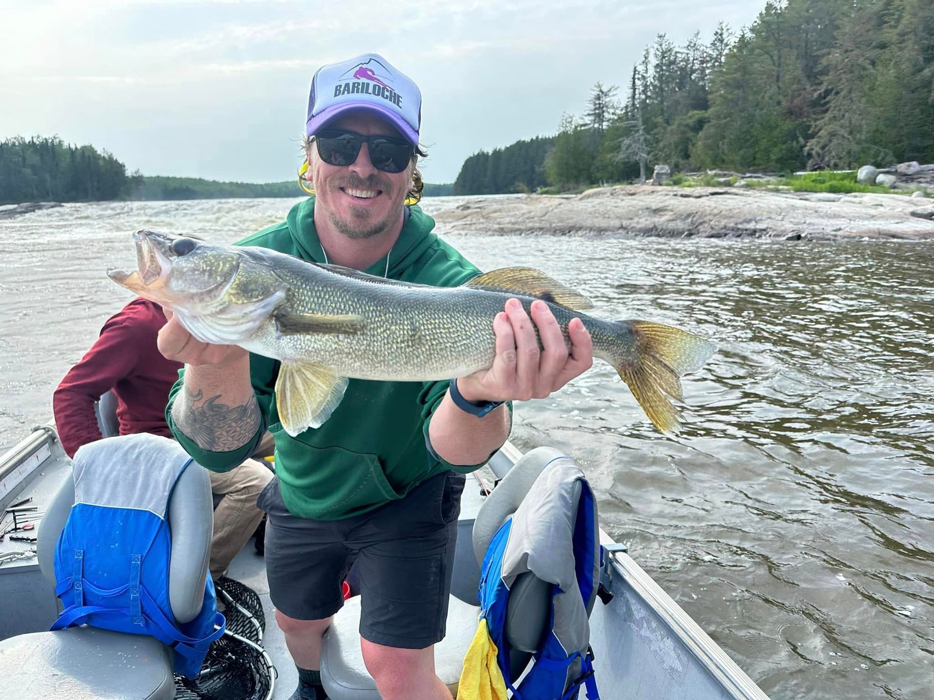 Behold a man in a boat proudly displaying a large walleye fish in his hands.