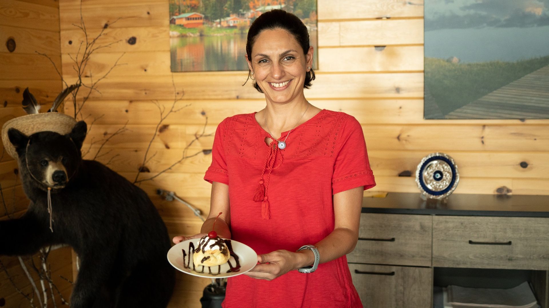 A woman in a red dress is holding a plate of food in front of a stuffed bear.