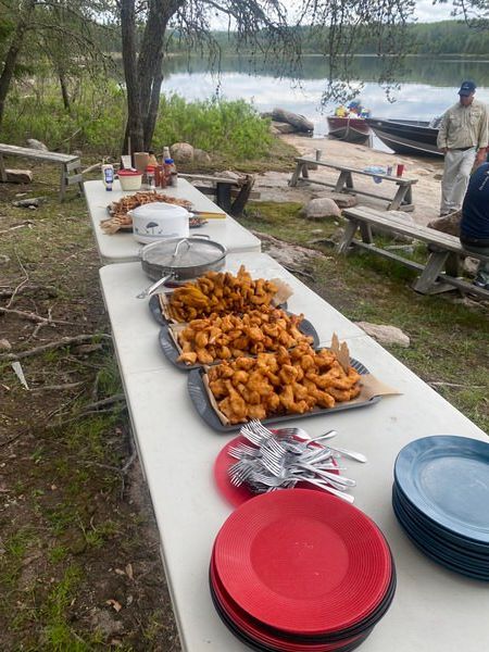 A long table with plates and utensils on it and fried walleye. 